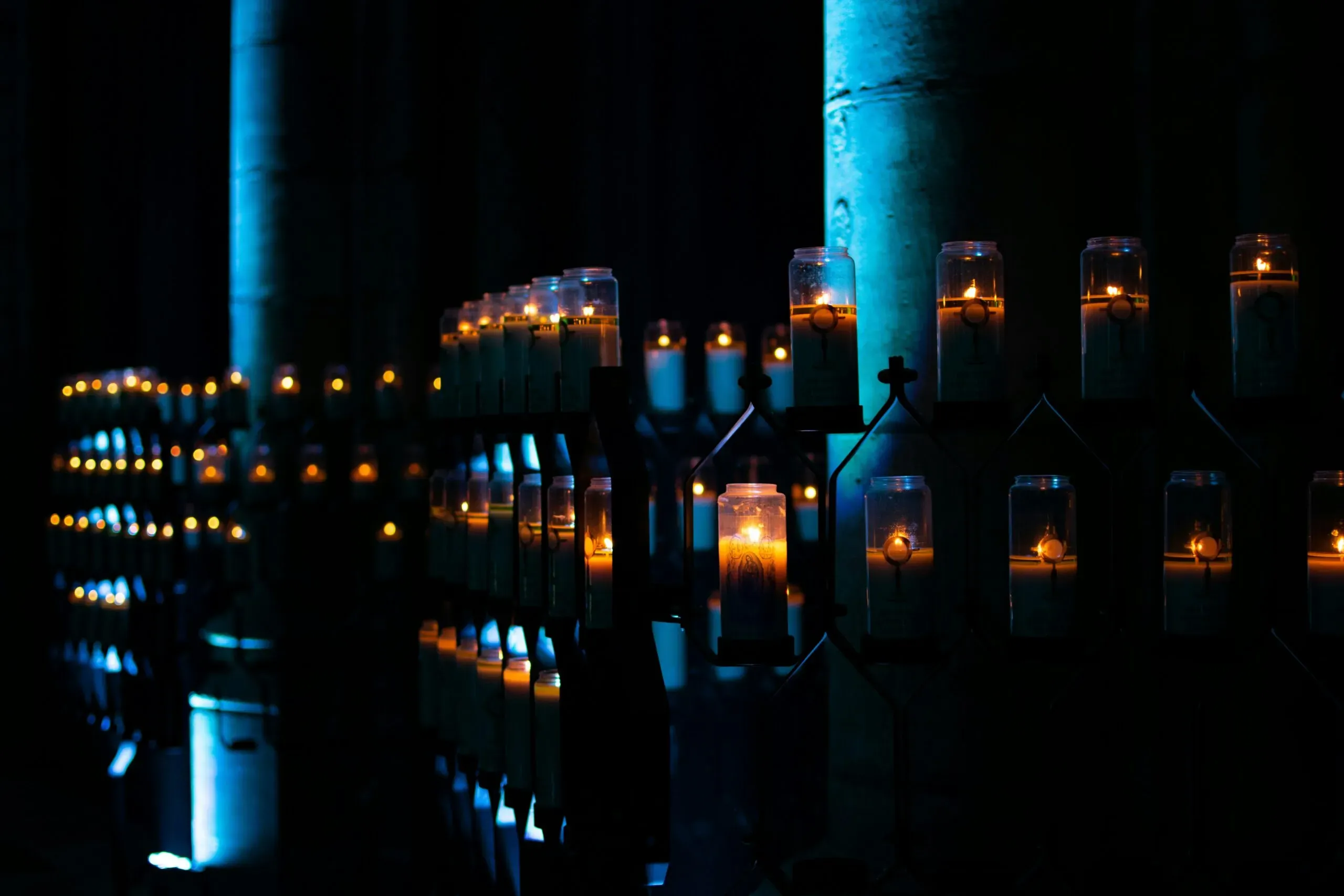 Rangées de bougies votives allumées dans la pénombre d'une église.