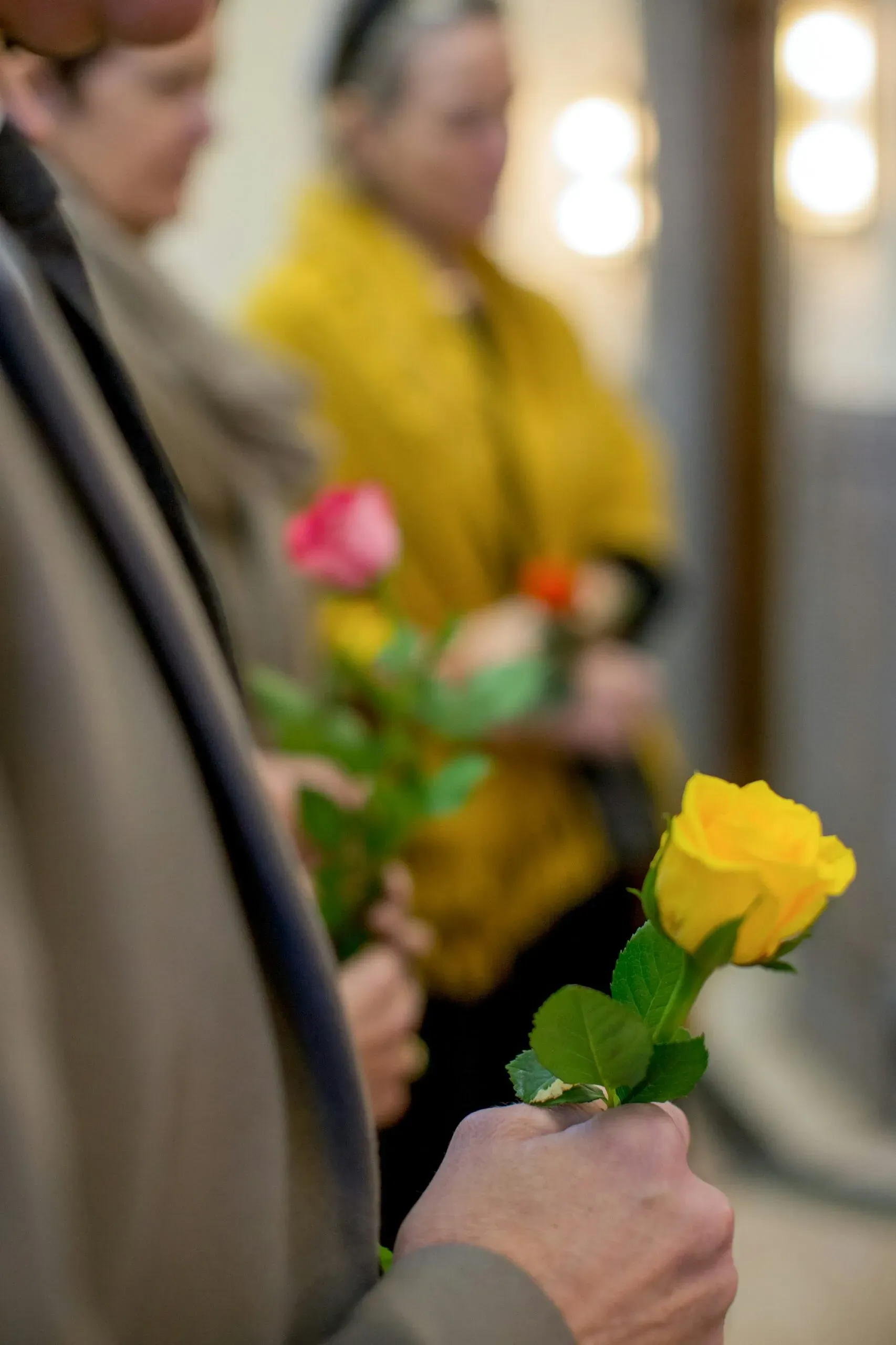 Mains tenant des roses roses et jaunes lors d'une cérémonie funéraire.